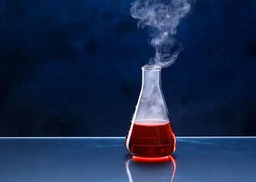 A glass flask with steaming red liquid inside of it.